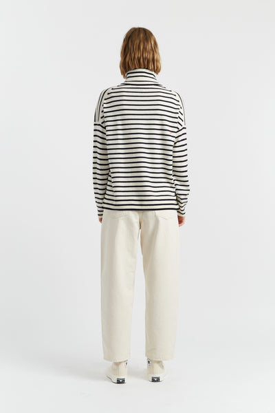 Person wearing a black and white striped sweater and beige pants on a white background