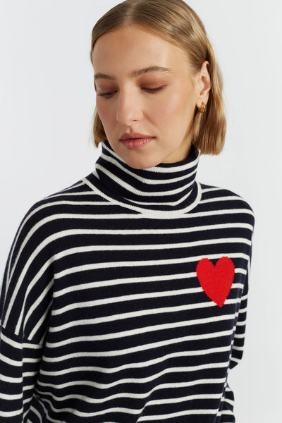 Woman wearing a black and white striped turtleneck with a red heart design on a light gray background