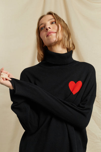 Person wearing a black turtleneck sweater with a red heart design on a beige background
