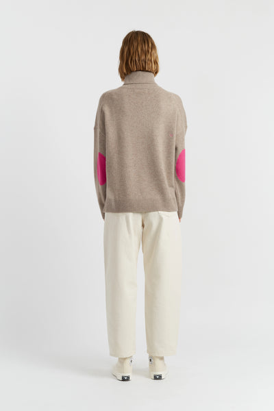 Person wearing a beige sweater with pink accents and white pants on a white background