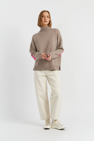 Person wearing a brown sweater with pink lining and white pants on a light gray background