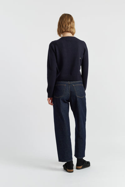 Person wearing a navy sweater and dark jeans on a white background