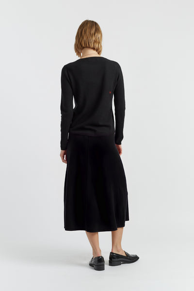 Person wearing a black long-sleeve top and black skirt on a white background