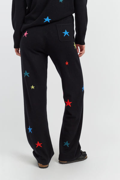 Black pants with colorful star patterns worn by a person on a white background