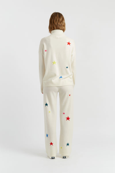 Person wearing a white outfit with colorful star patterns on a plain background
