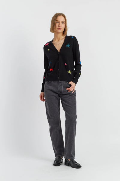 Person wearing a black cardigan with colorful star patterns and gray jeans on a white background