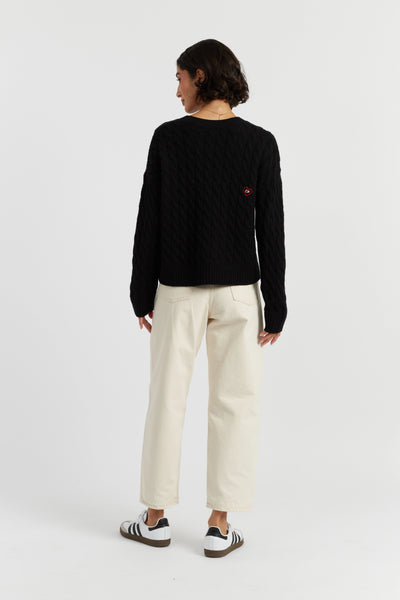 Person wearing a black sweater with a red logo and white pants on a white background