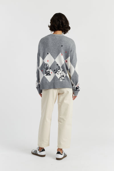 Person wearing a gray sweater with geometric pattern and white pants on a white background