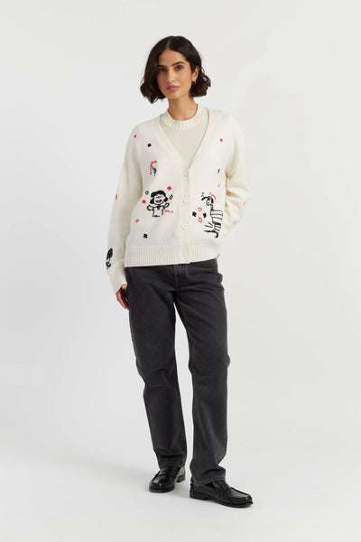Woman wearing a white cardigan with black and red designs, paired with dark jeans and black shoes on a white background.