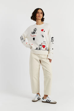 Person wearing a white sweater with graphic designs and beige pants on a white background