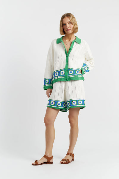 Woman wearing a white cardigan with green and blue patterns on a white background