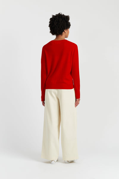 Person wearing a red sweater and white pants on a white background