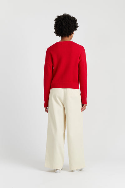 Person wearing a red sweater and white pants on a white background