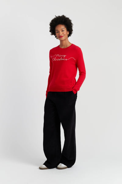 Person wearing a red 'Merry Christmas' sweater and black pants on a white background