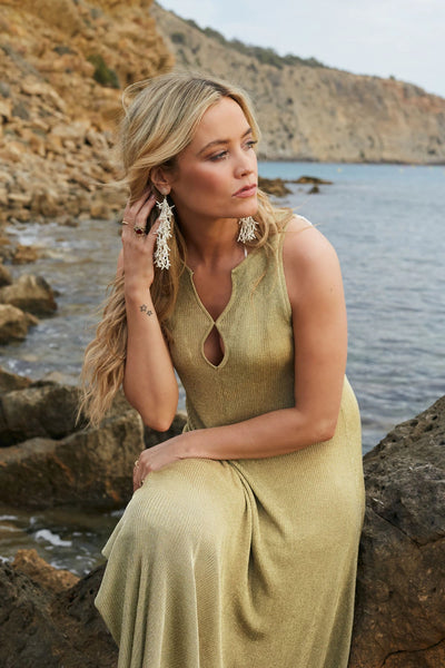 Woman in a yellow dress sitting by a rocky coastline with water in the background