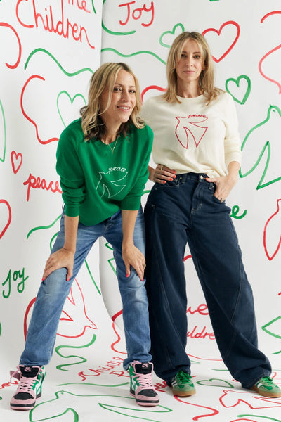 Two women posing against a colorful wall with hearts and text.