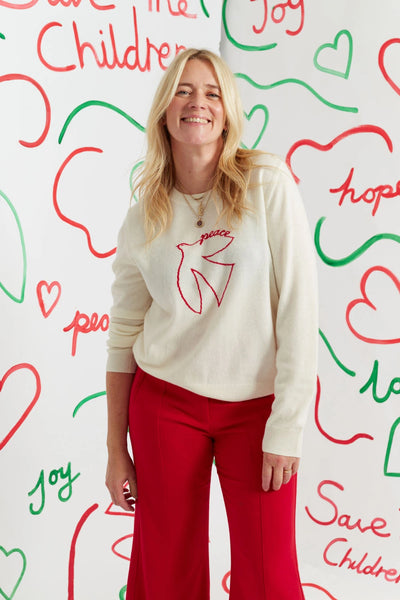 Woman wearing a white sweater with a red design in front of a colorful wall with text and hearts.