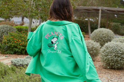 Person wearing a green jacket with 'Peanuts' and Snoopy graphics outdoors.