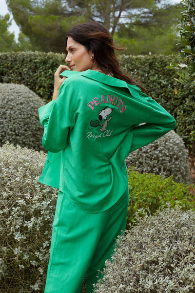 Person wearing a green 'Peanuts' robe in an outdoor setting with bushes and trees.
