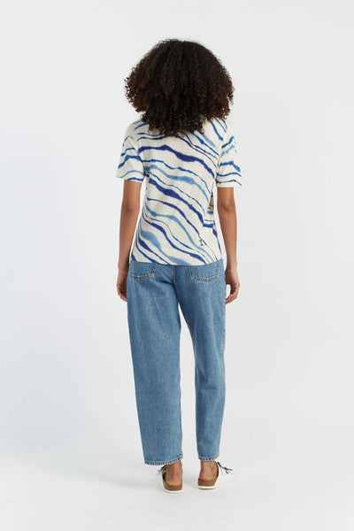 Person wearing a patterned shirt and blue jeans on a white background