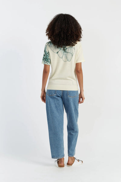 Person wearing a cream t-shirt with a graphic design and blue jeans on a white background