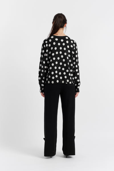 Person wearing a black polka dot blouse and black pants on a white background