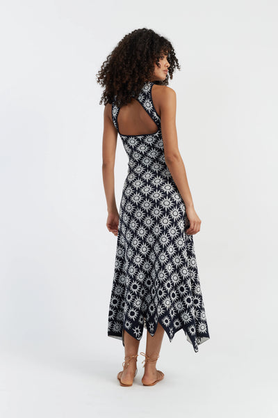 Woman in a navy blue dress with white patterns standing against a plain background. 