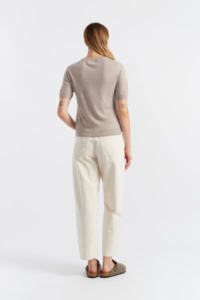 Woman wearing a beige sweater and white pants on a white background