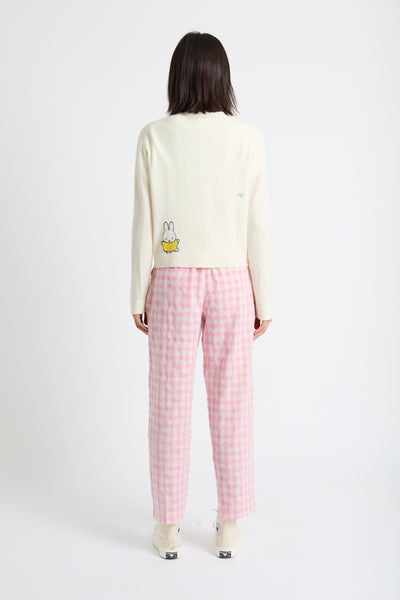 Person wearing a cream long-sleeve shirt with a graphic and pink checkered pants on a white background