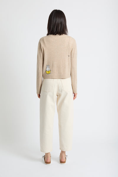Woman wearing a beige sweater with a character design on a white background