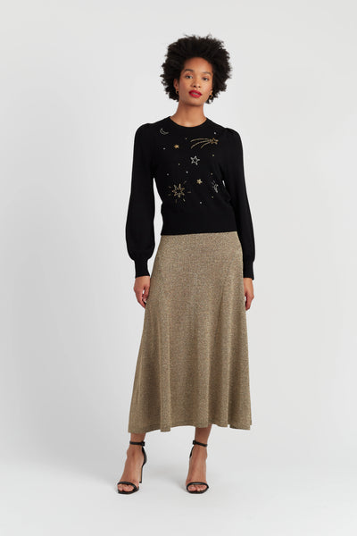 Woman wearing a black sweater with gold designs and a beige skirt on a white background