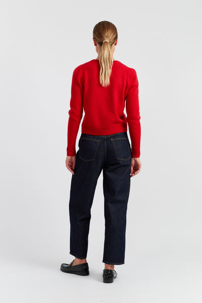Person wearing a red sweater and dark jeans on a white background