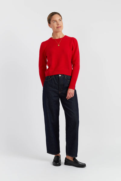 Woman wearing a red sweater and dark jeans on a white background