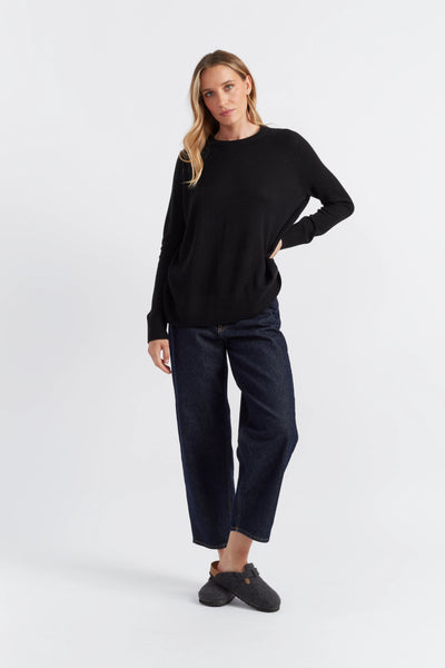 Woman wearing a black sweater and dark jeans on a white background