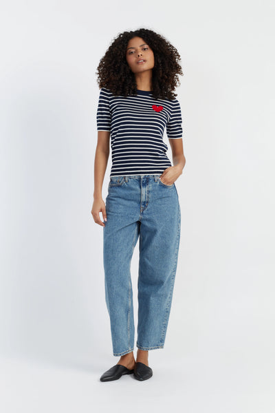 Woman wearing a striped shirt with a red heart and blue jeans on a white background