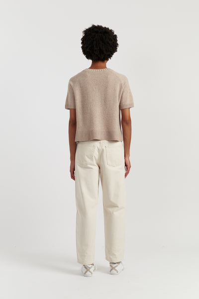 Person wearing a beige sweater and white pants on a white background