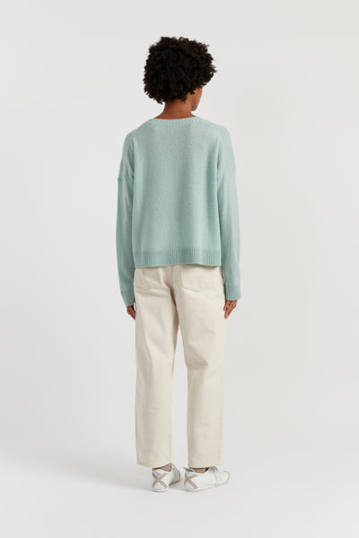 Person wearing a light green sweater and beige pants on a white background