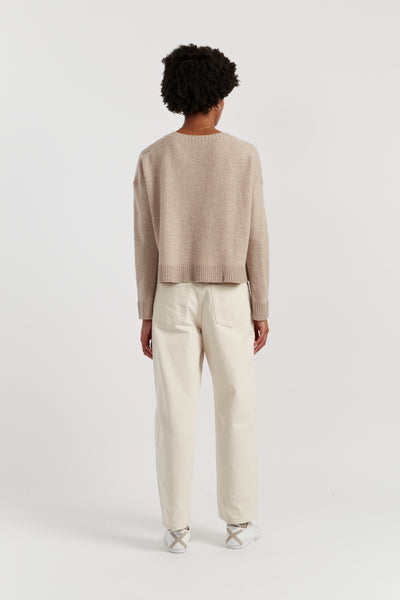 Person wearing a beige sweater and white pants on a light background