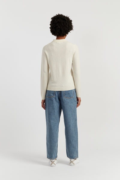 Person wearing a cream sweater and blue jeans on a white background