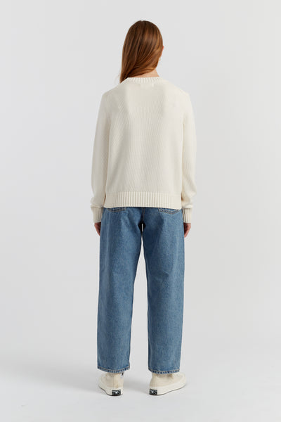 Person wearing a cream sweater and blue jeans on a white background