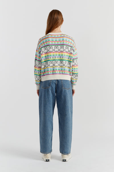 Person wearing a colorful patterned sweater and blue jeans on a white background