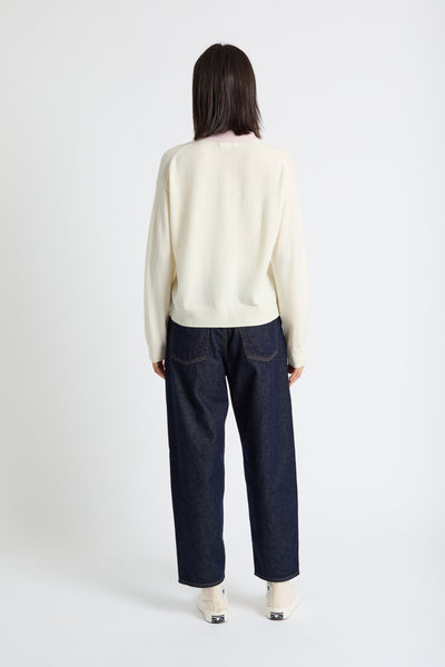 Person wearing a cream sweater and dark blue jeans on a white background