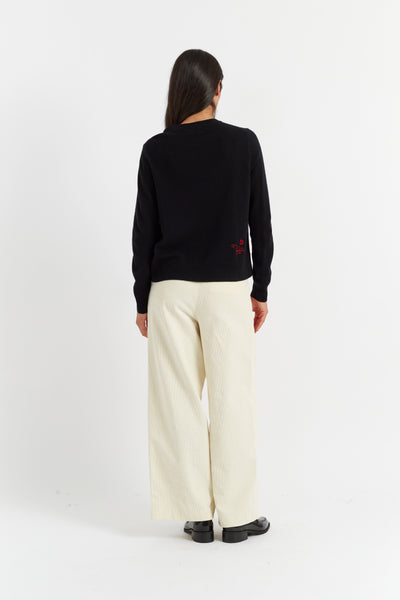 Person wearing a black sweater and white pants on a white background