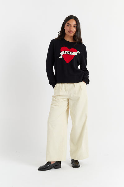 Woman wearing a black sweater with a red heart design and white pants on a white background