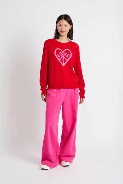 Person wearing a red sweater with a heart design and pink pants on a white background