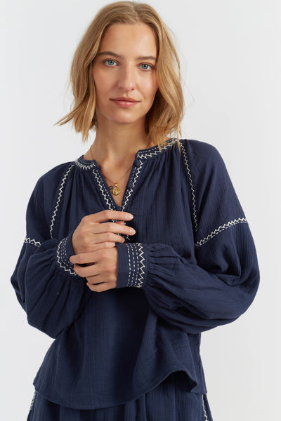 Woman wearing a navy blue blouse with intricate white embroidery on a white background