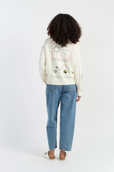 Person wearing a white sweater with colorful designs and blue jeans on a white background