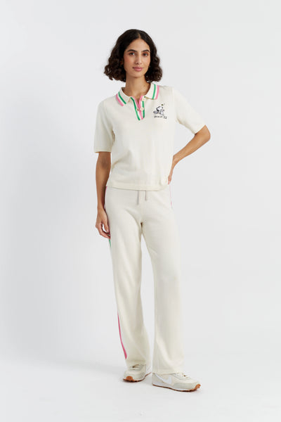 Woman wearing a white cricket uniform with a logo on a white background