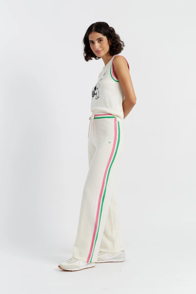 Woman wearing a white sleeveless top and cream pants with red and green stripes on a white background