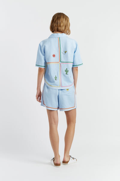 Woman wearing a light blue embroidered outfit on a white background